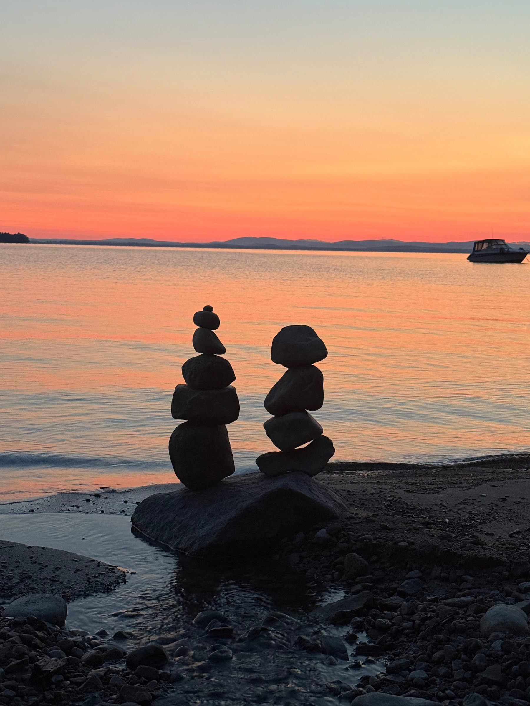 Stone cairns on the beach at Camp Two Step at sunset, with a boat moored on Lake Champlain